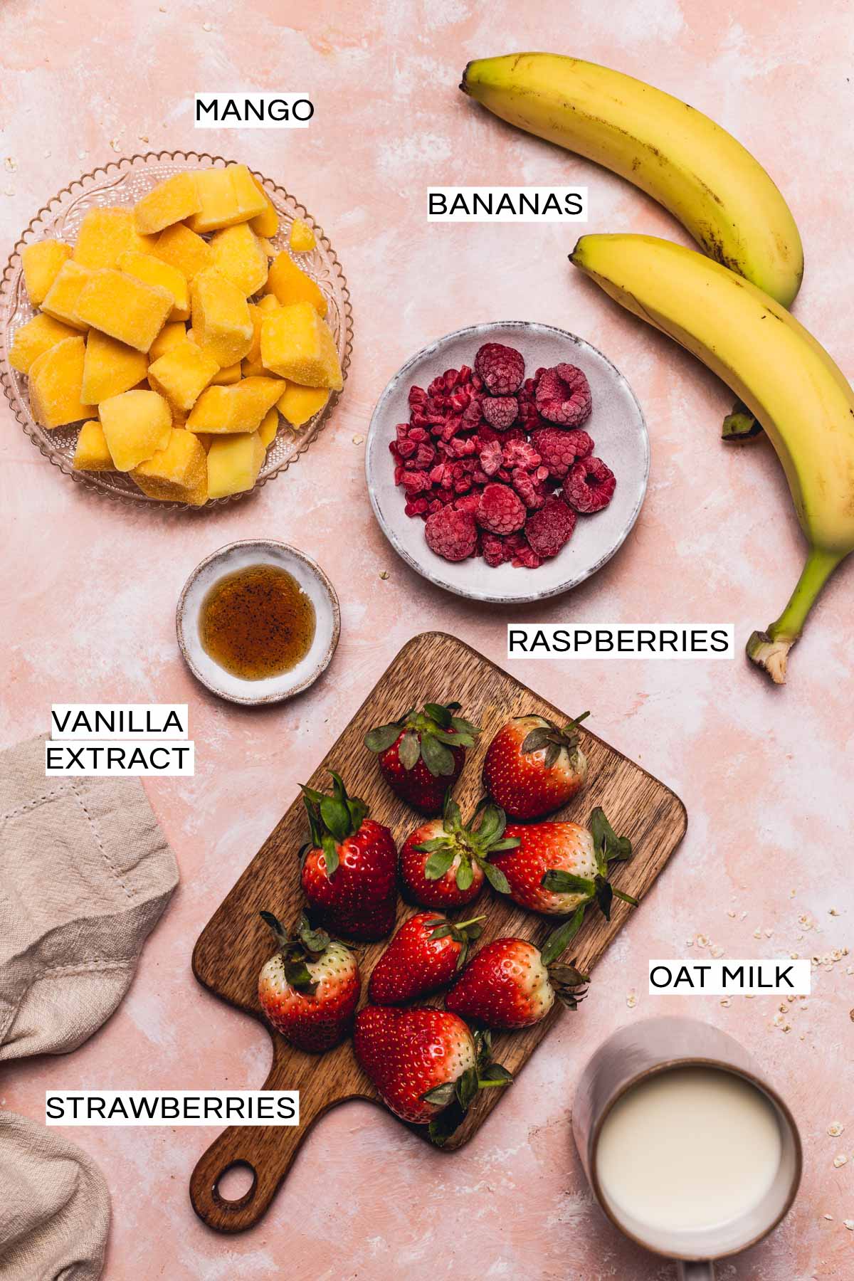 An overhead view of various ingredients needed to make an oat milk fruit smoothie placed on a flat surface. 