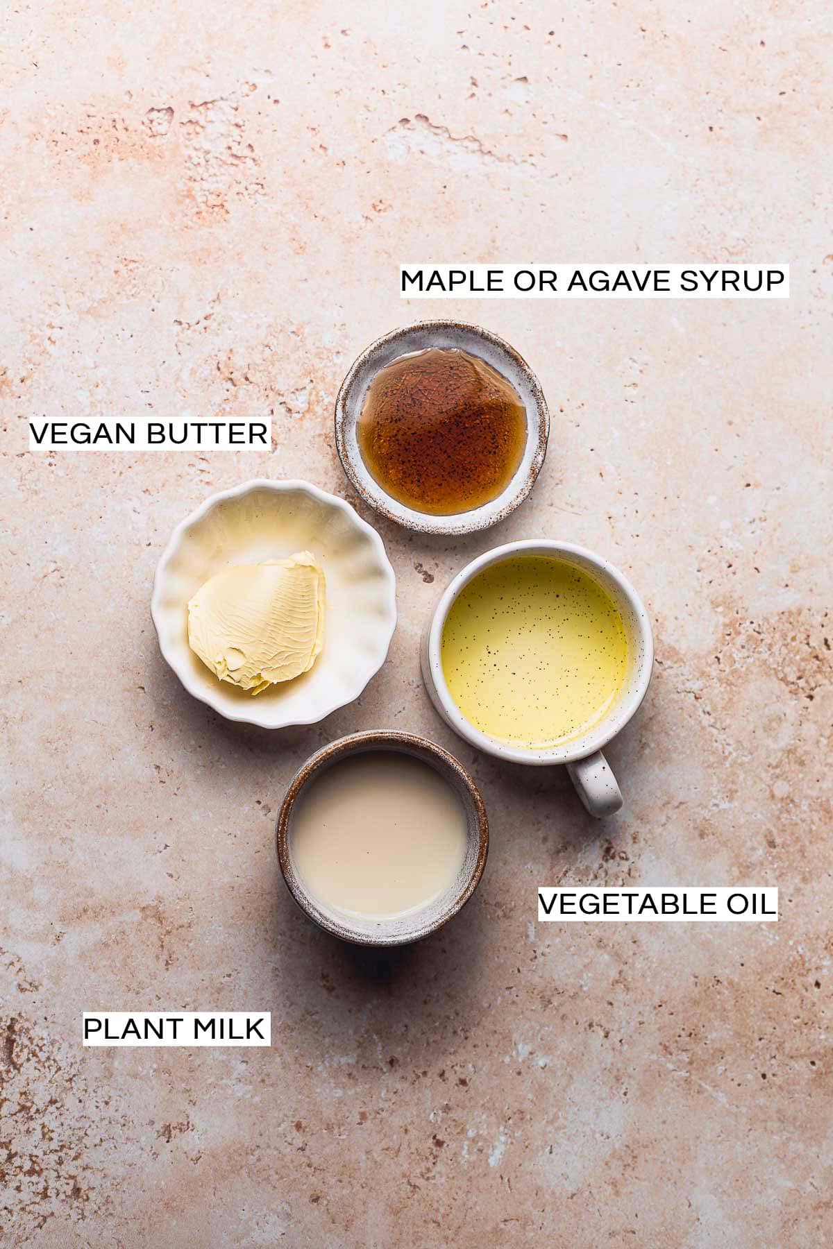 Four staple vegan egg wash ingredients in bowls on a rusty background.