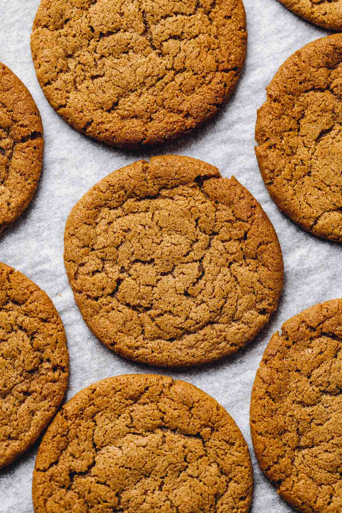 A close up image of several vegan ginger cookies with a cracked top on a sheet of baking paper.