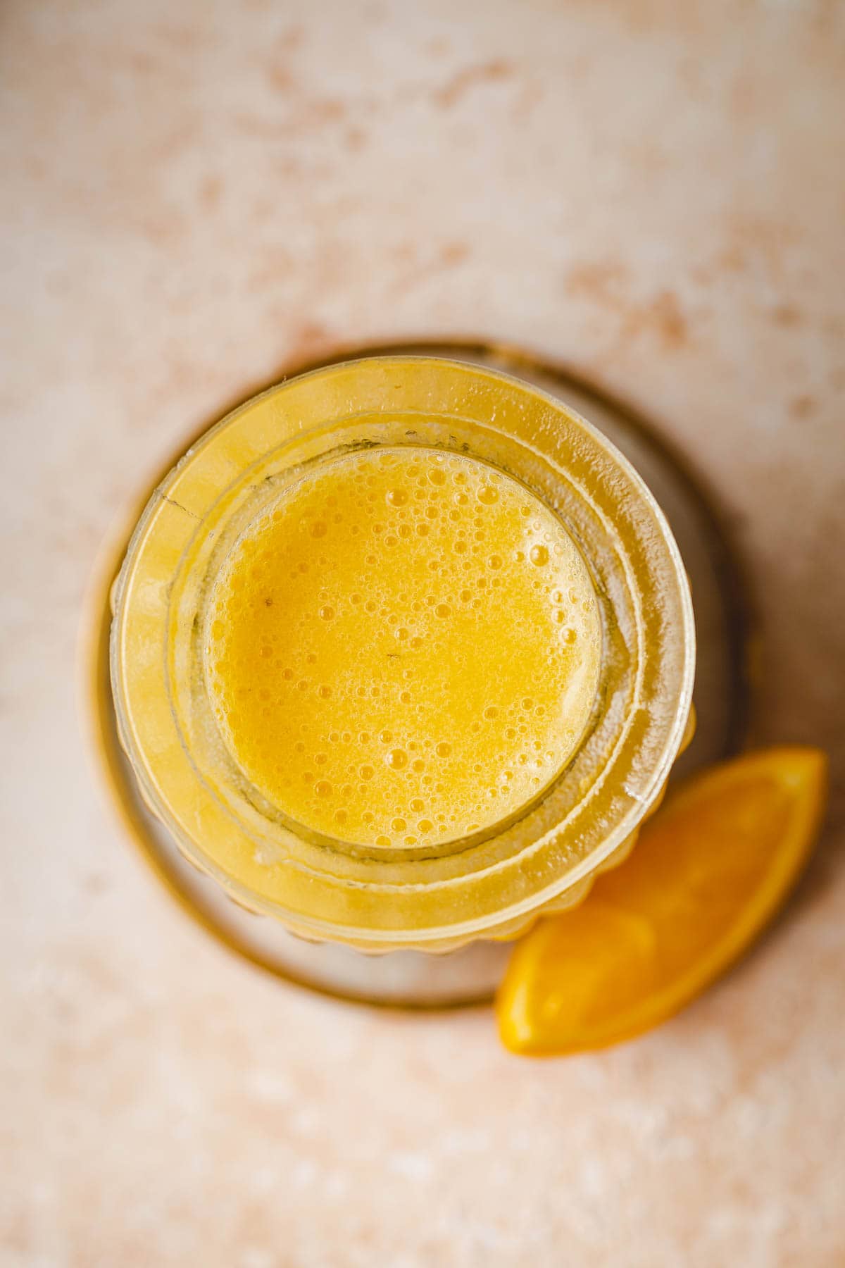 A close-up overhead image of a yellow smoothie in a glass.