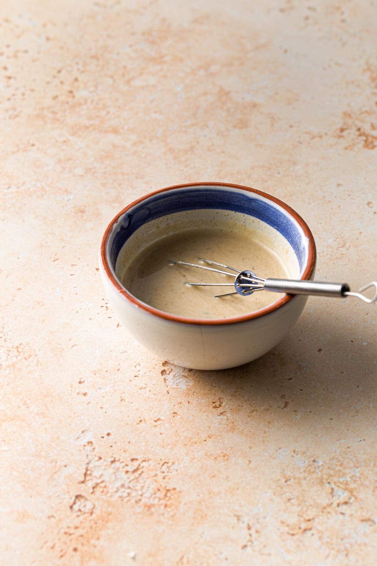 A small bowl of tahini with a whisk placed in the middle.
