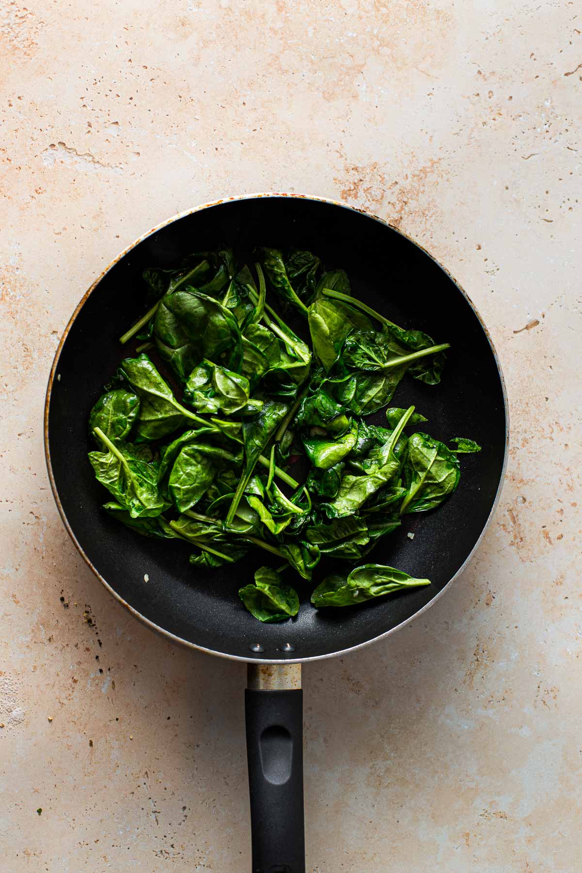A large black frying pan filled with wilted spinach.
