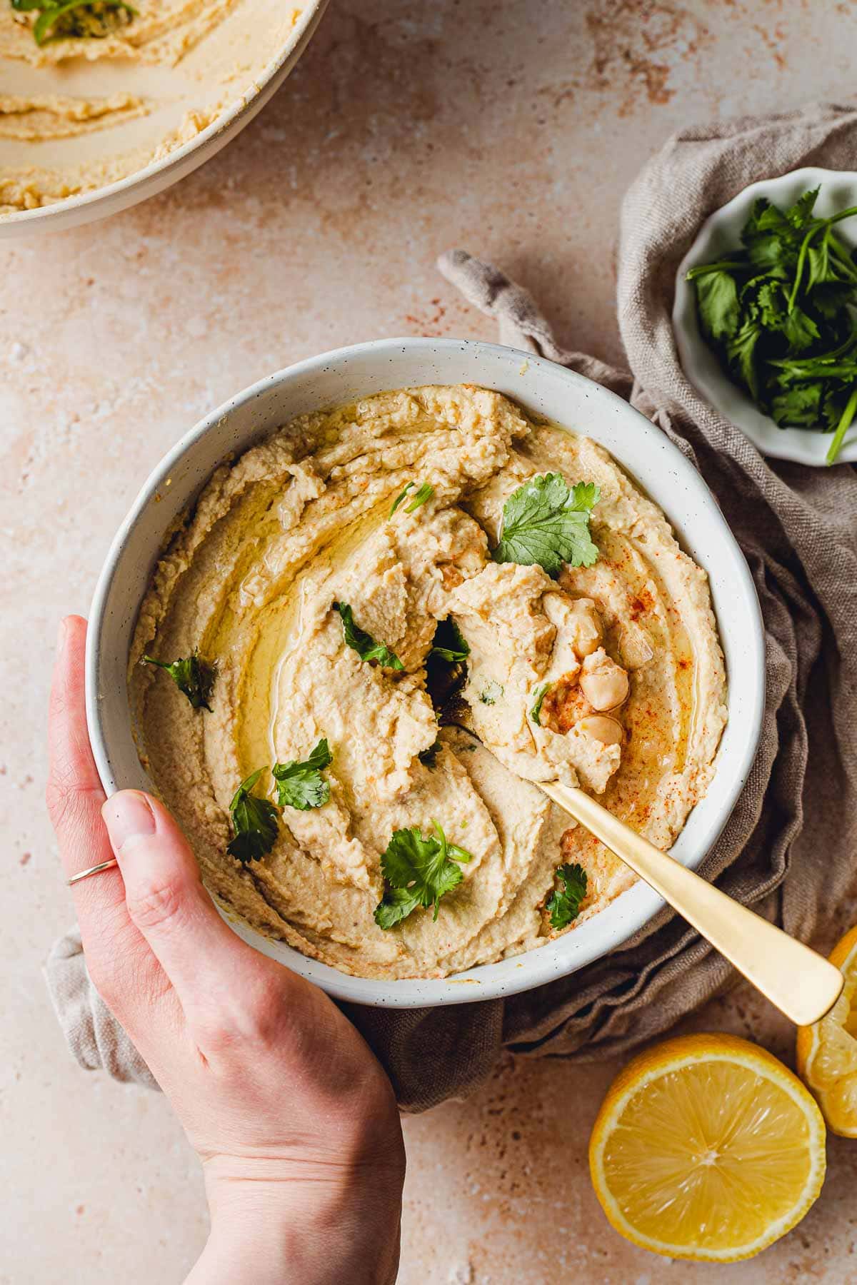 A bowl full of hummus with a hand holding the side of the bowl.
