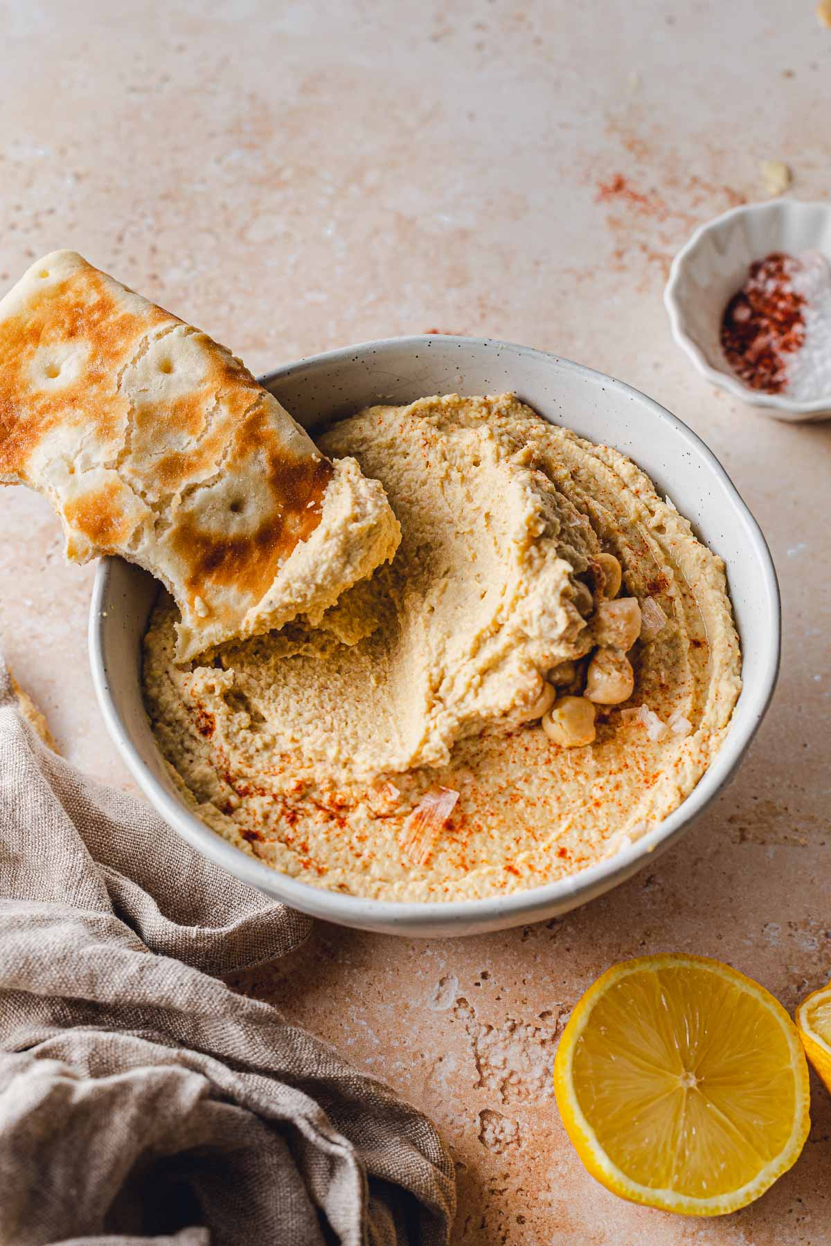 Hummus in a large bowl with a piece of bread placed in it.