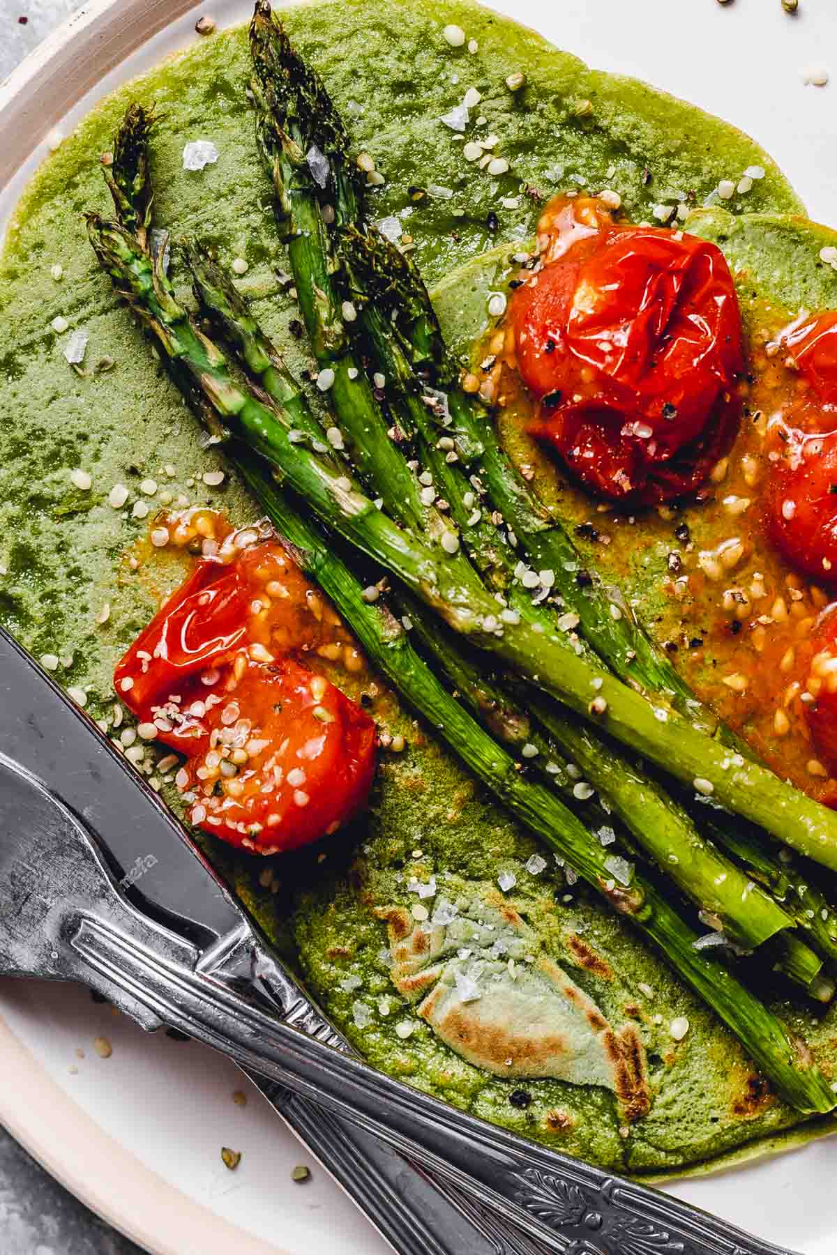 A close-up view of a crepe topped off with tomatoes and asparagus.