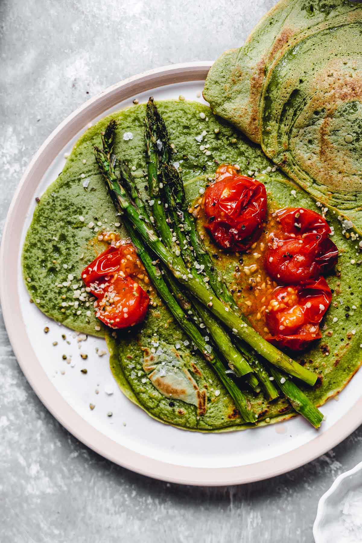 A close-up overhead view of the spinach crepes topped off with tomatoes and asparagus.