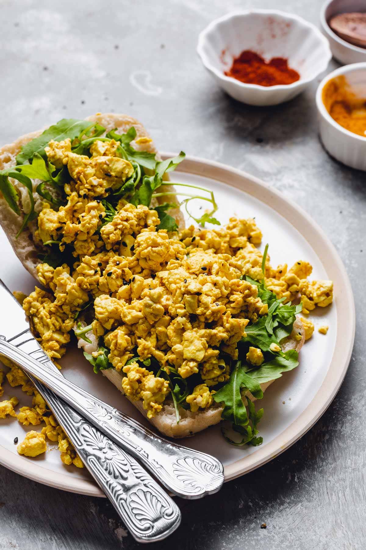 An open bread topped off with tofu and arugula on a plate.