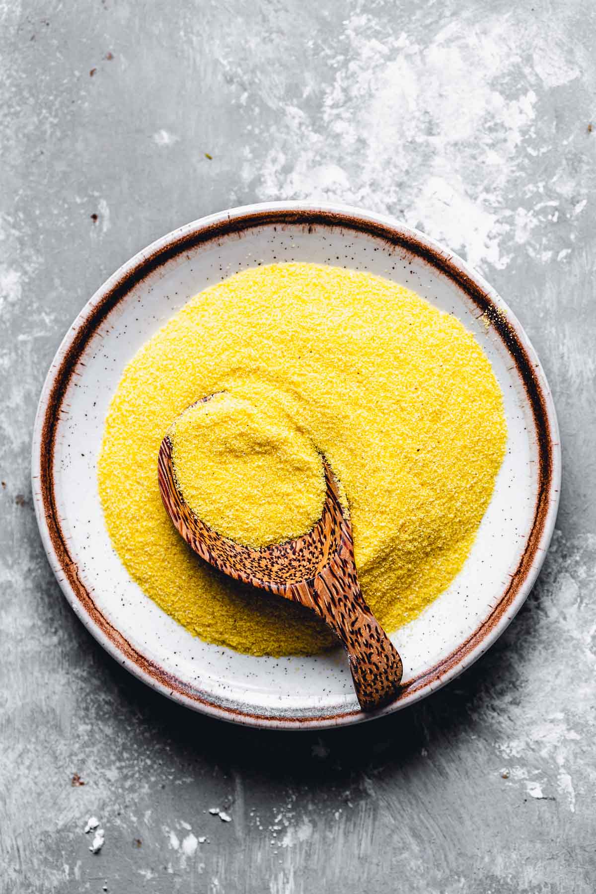 A small ceramic plate filled with cornmeal, with a wooden spoon placed in the middle.