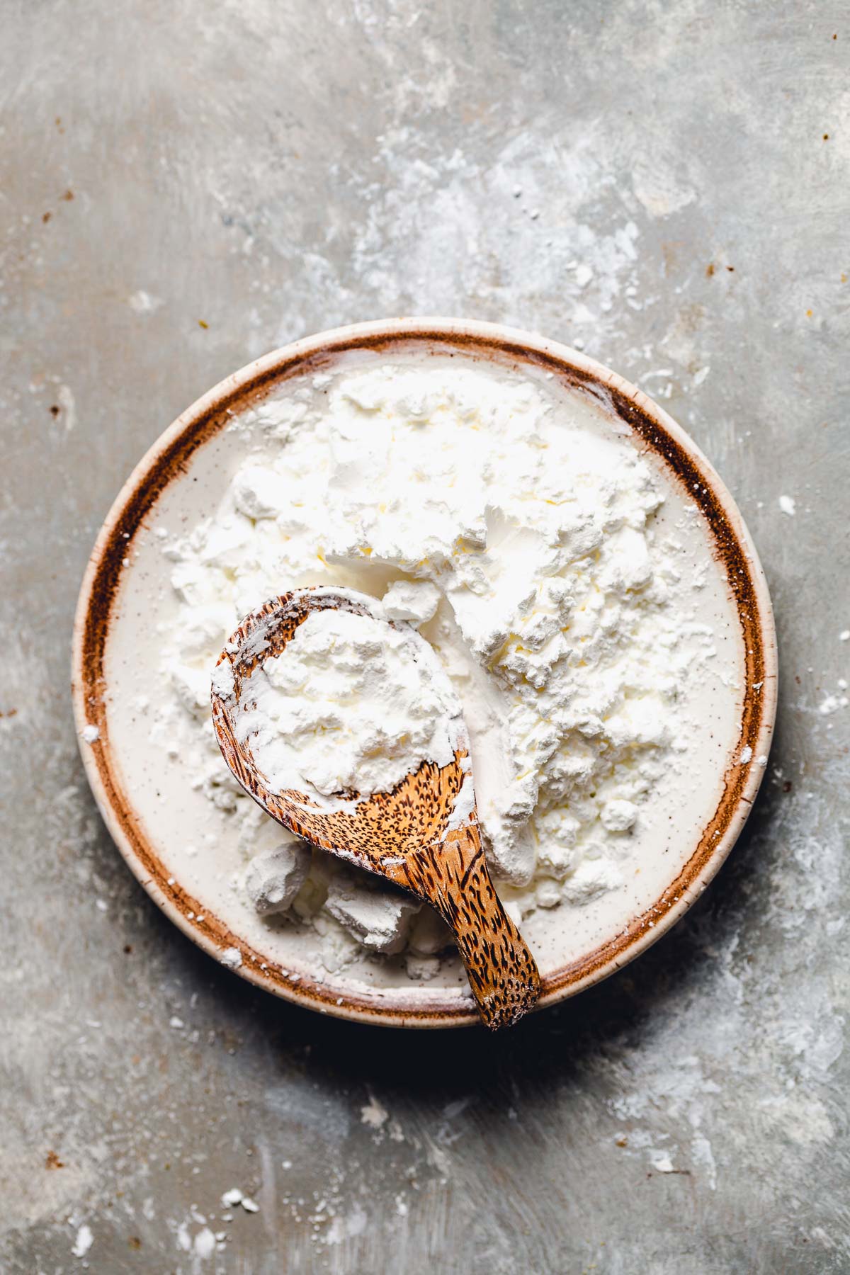 A small ceramic plate filled with cornstarch, with a wooden spoon placed in the middle.