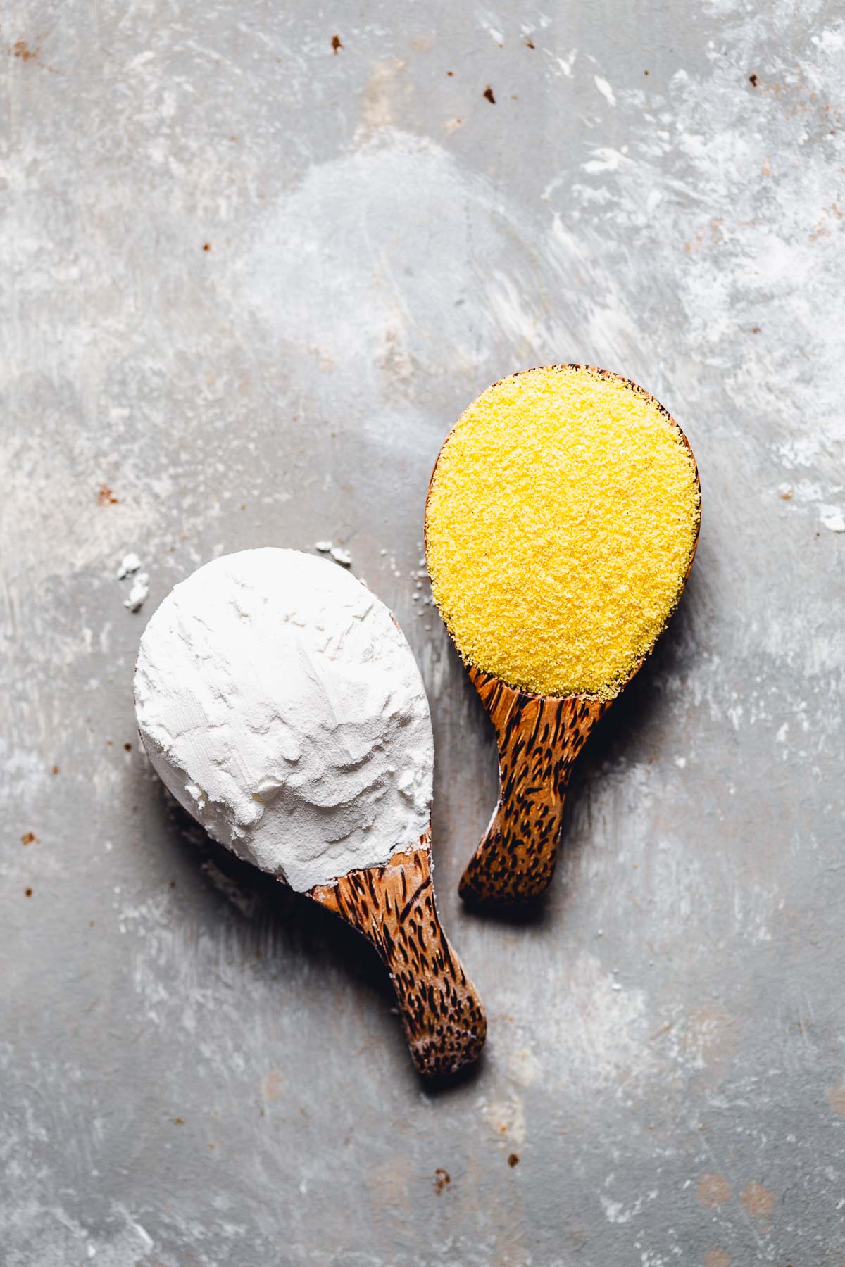 Two wooden spoons, one with cornstarch and one with cornmeal.