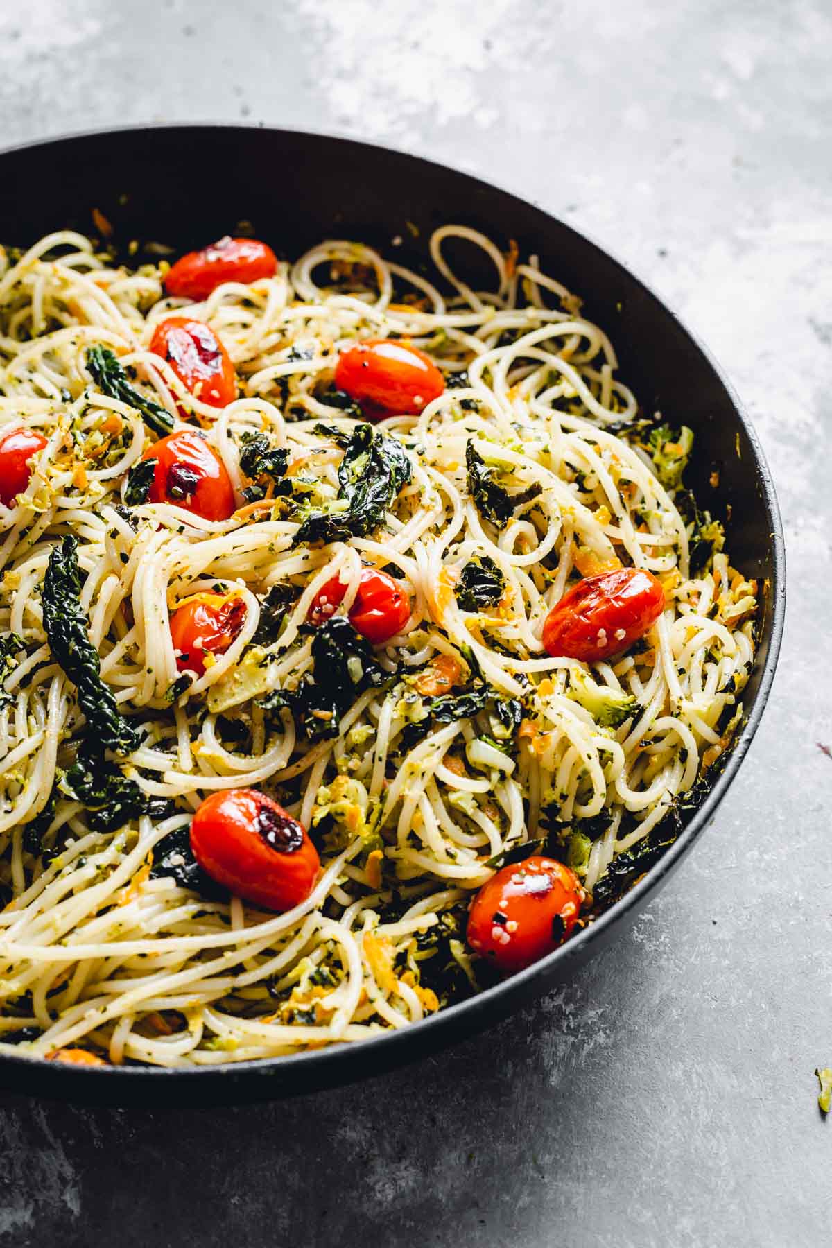 A side view of cavolo nero pasta with small plum tomatoes in a large black pan.
