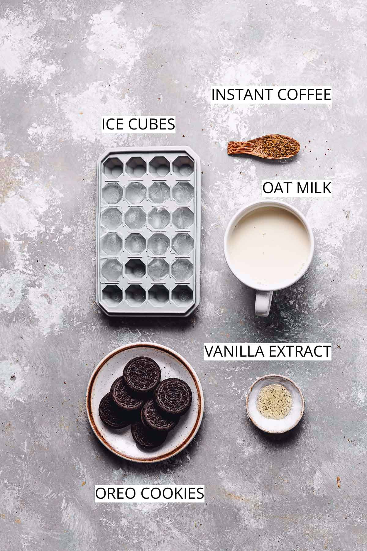 Ice cubes, instant coffee, milk, vanilla, and Oreo cookies on a flat surface.