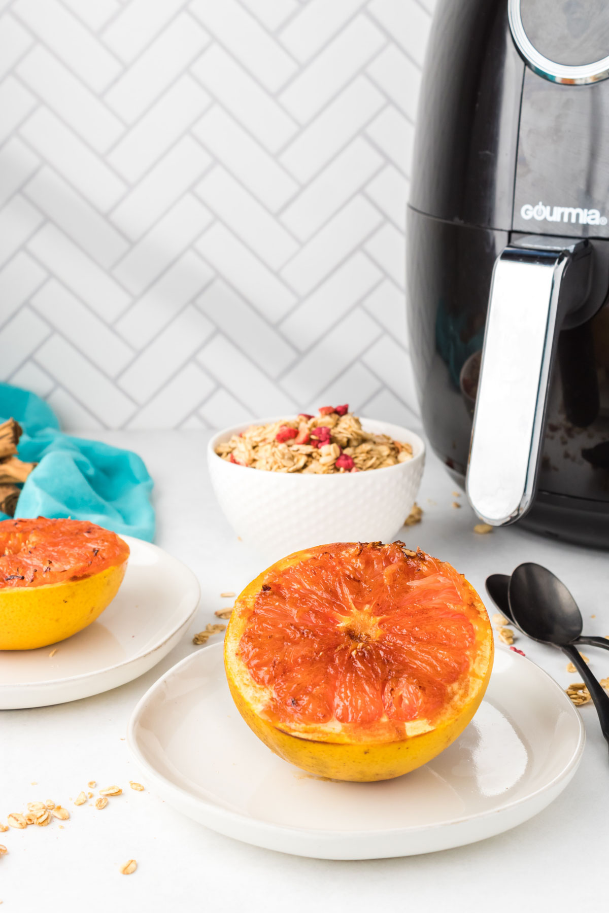 Half of a grapefruit placed on a round plate in front of a large Gourmia air fryer in the back. 