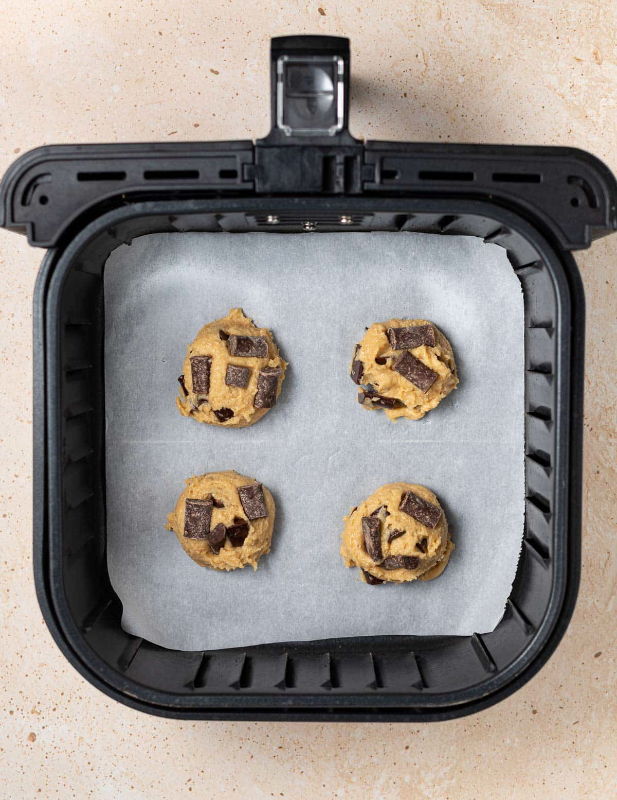 An overhead view of an open air fryer containing four cookies placed on a parchment paper. 