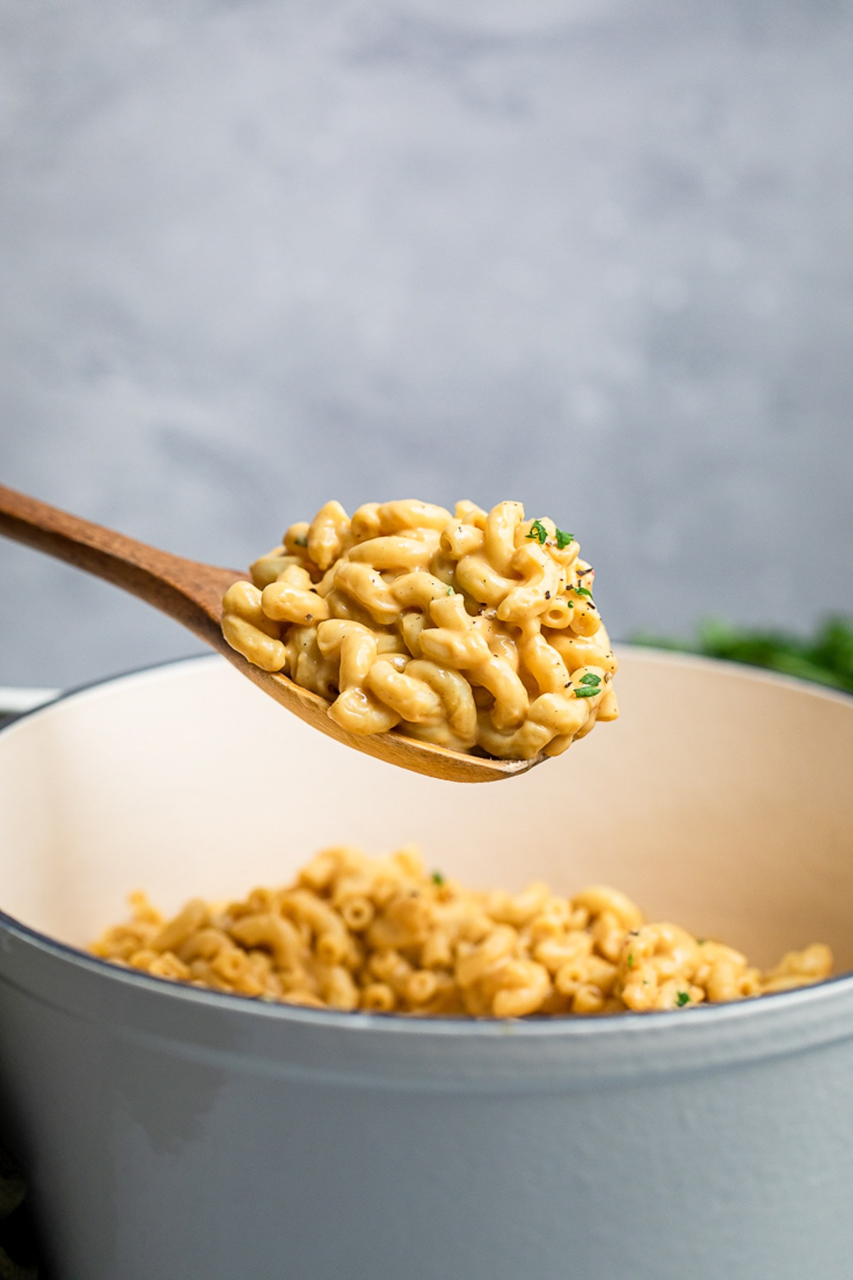A wooden spoon lifting simple vegan mac and cheese from a pan.