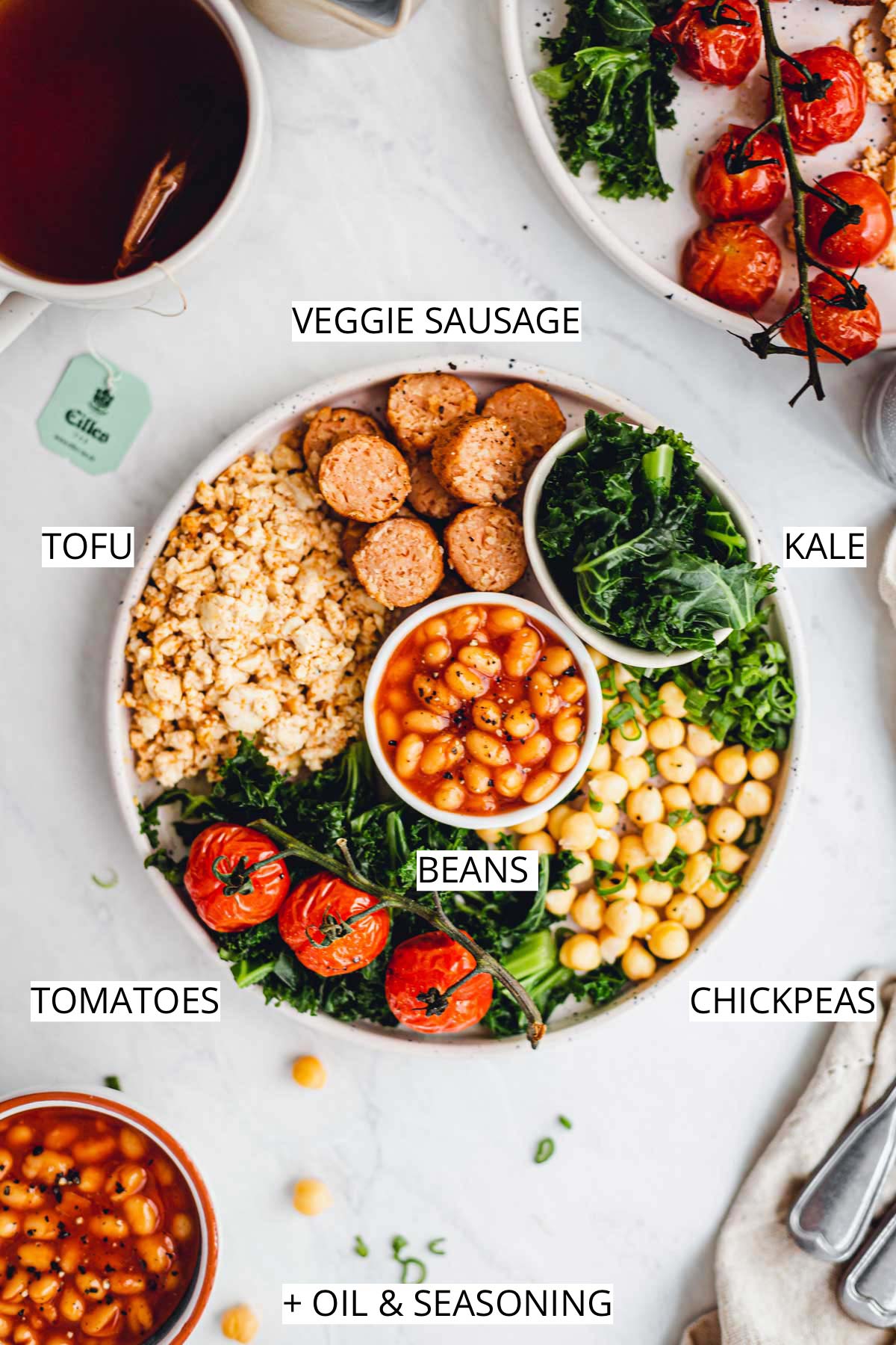 A plate filled with English vegan breakfast including tofu scramble, baked beans, sausages, tomato, annd kale.