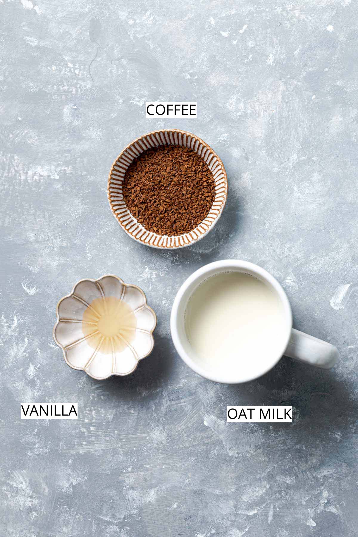 Three ingredients (oat milk, coffee, vanilla) needed to make oat milk latte placed on a flat grey surface. 