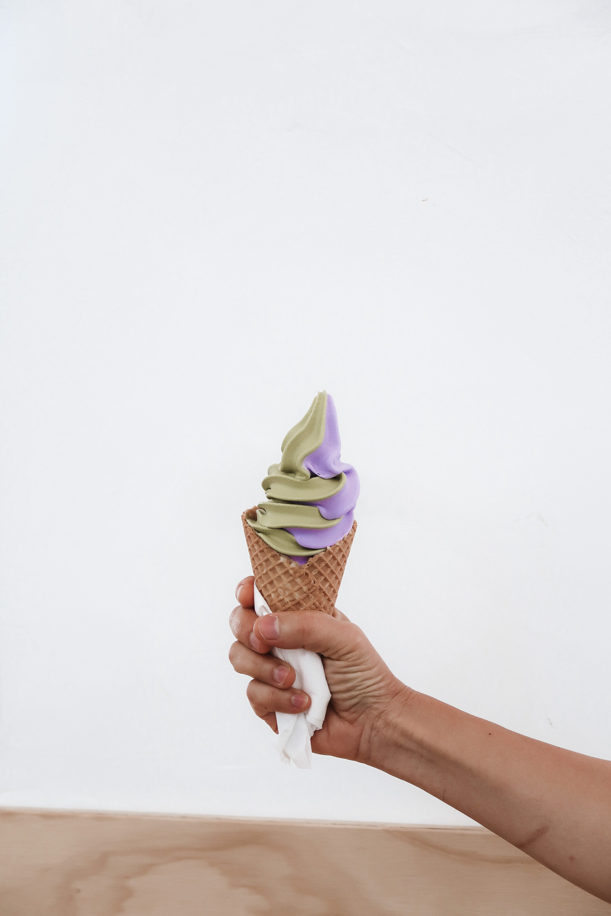 A hand holding out a cone with matcha and taro soft serve ice cream.
