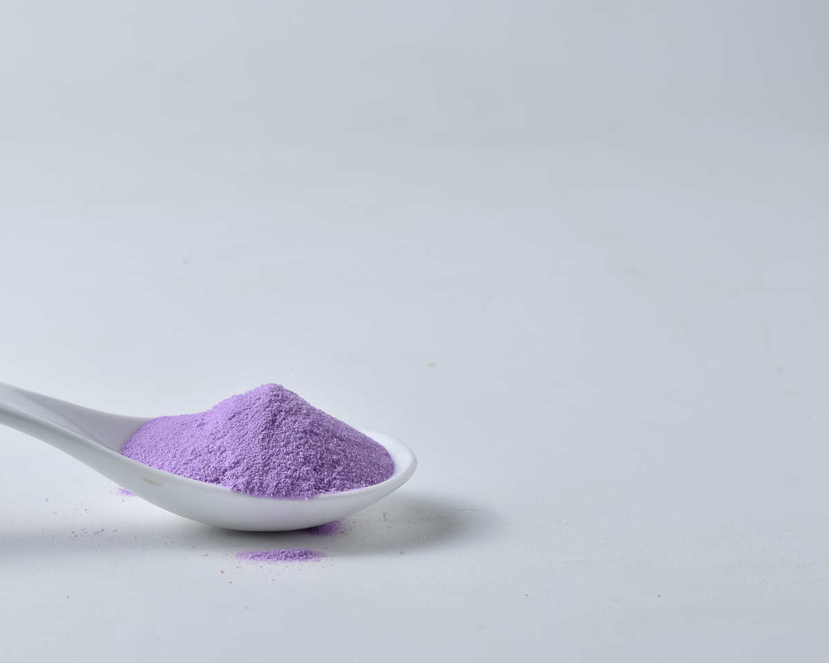 A spoon containing purple taro powder on a plain white background.