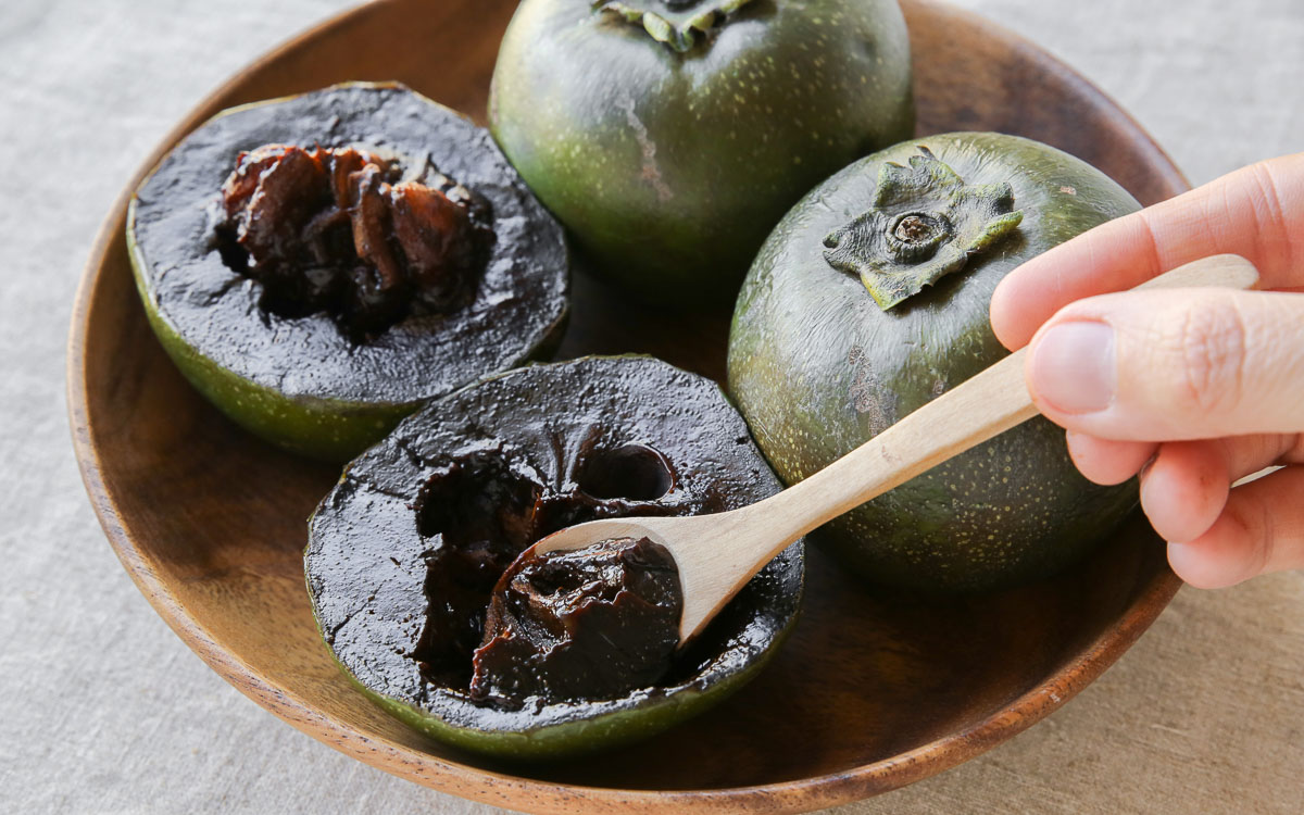 A hand reaching out to spoon black sapote from a wooden basket.