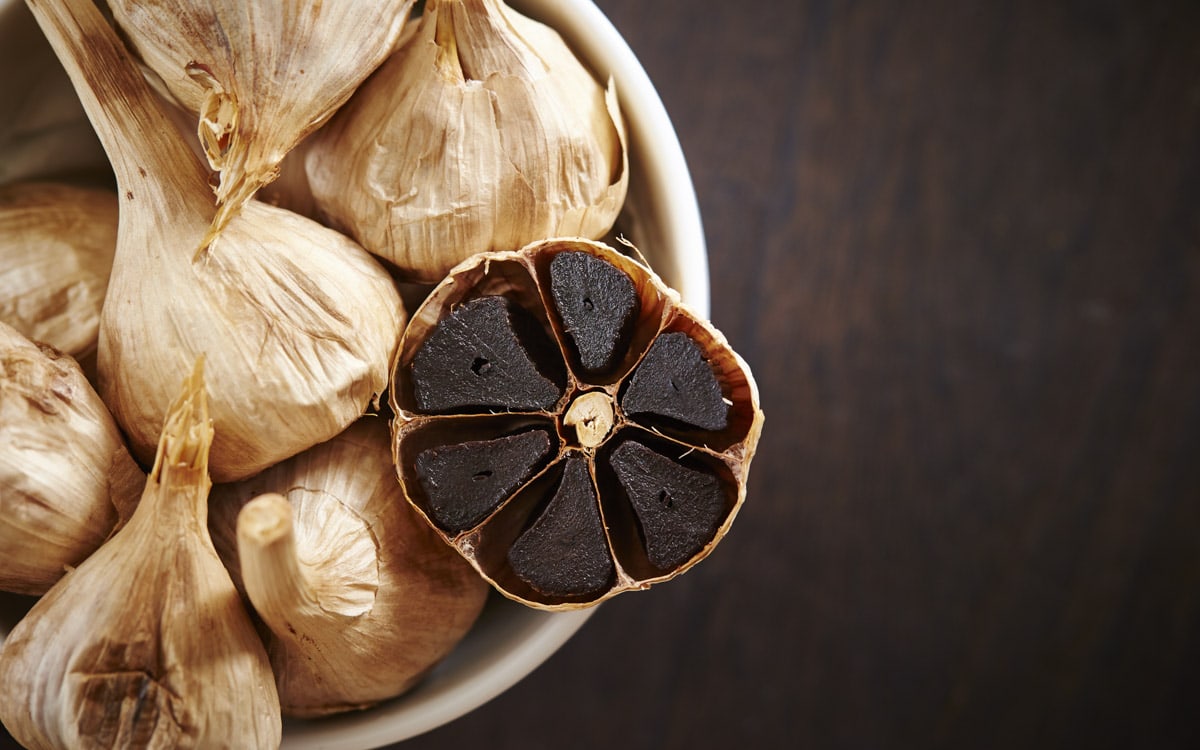 A bowl of black garlic placed on a dark wooden background.