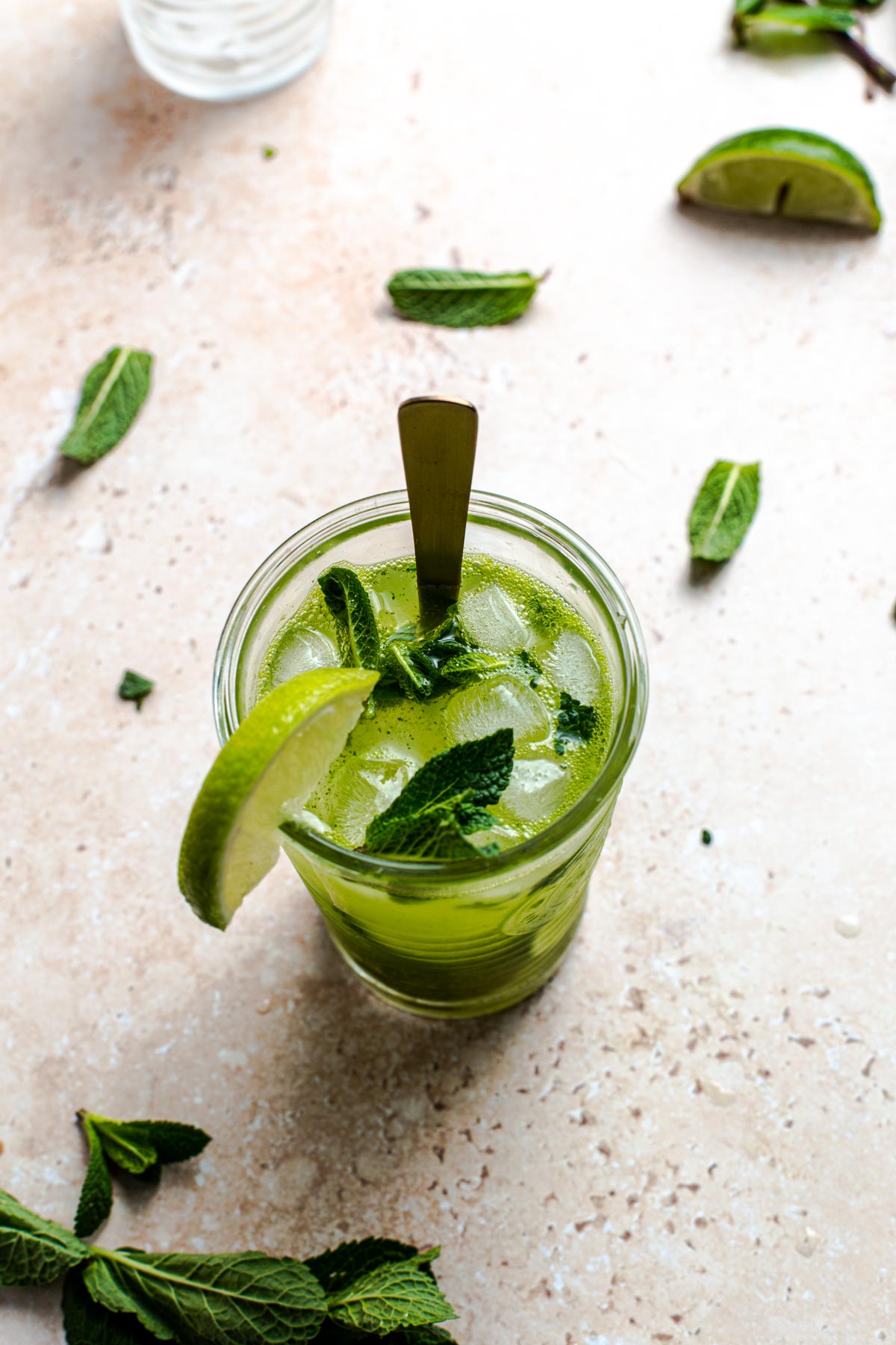 A glass of Thermomix mojito placed on a flat surface with mint leaves and lime wedges around it.