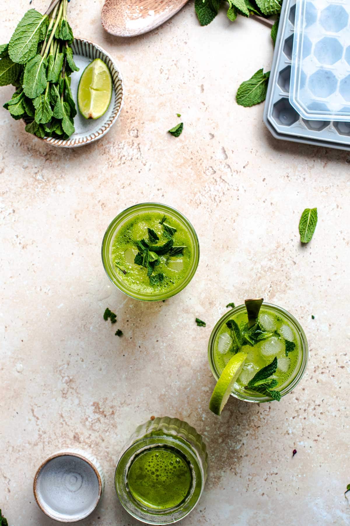 A table setting featuring two glasses of mojito and various ingredients scattered around it.