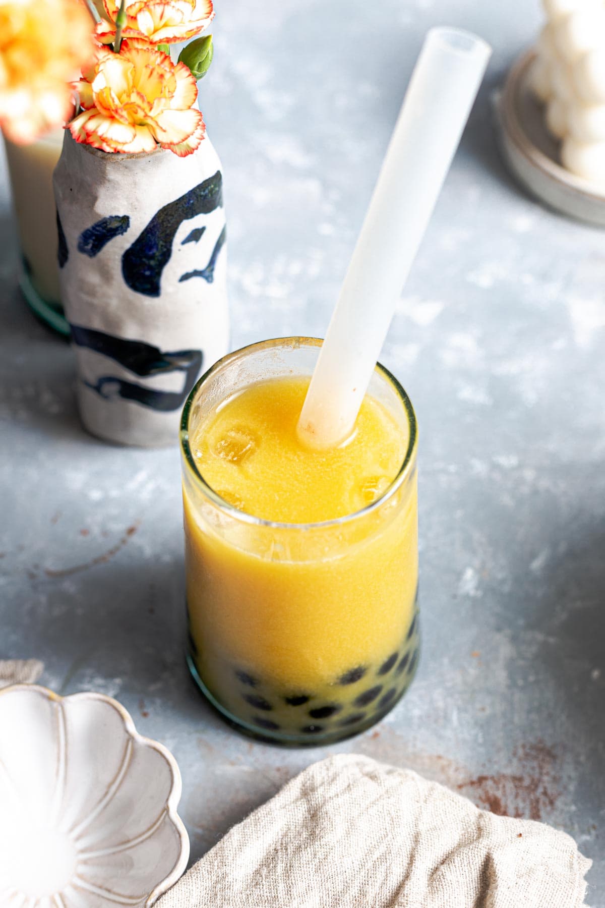 A large glass filled with mango milk tea with tapioca pearls and a straw.