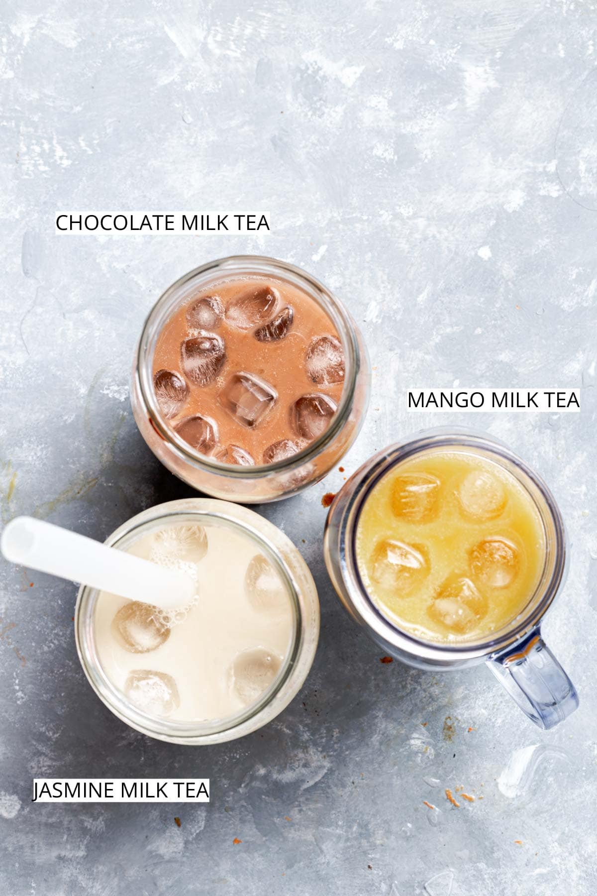 Three variations of milk tea next to each other on a flat grey surface.