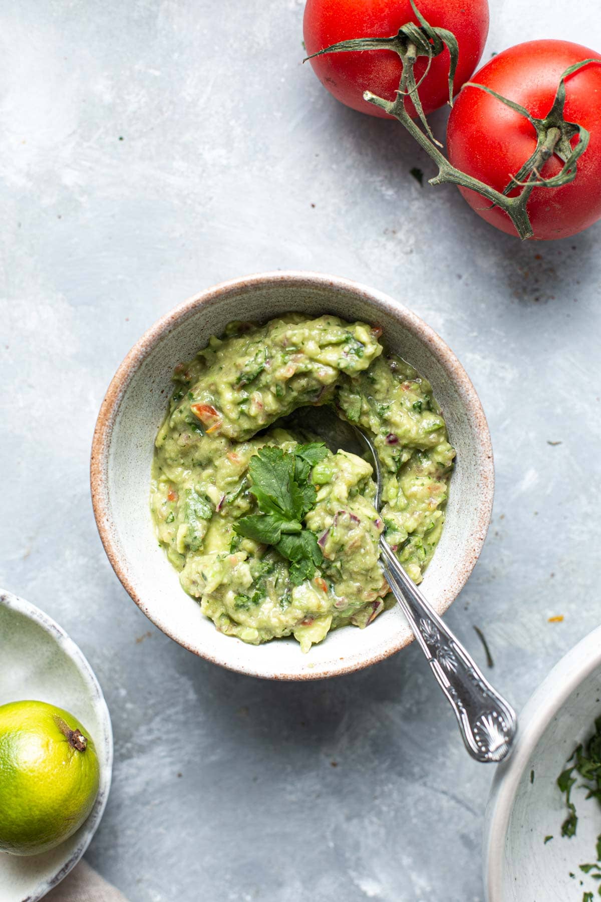 A bowl of fresh Guacamole with a spoon inserted in the middle and topped off with cilantro.