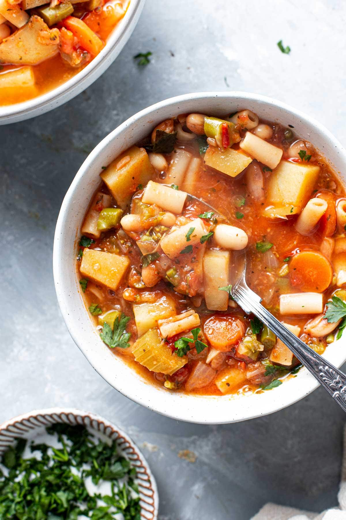 A close-up image of a bowl of minestrone with a spoon placed in the middle.