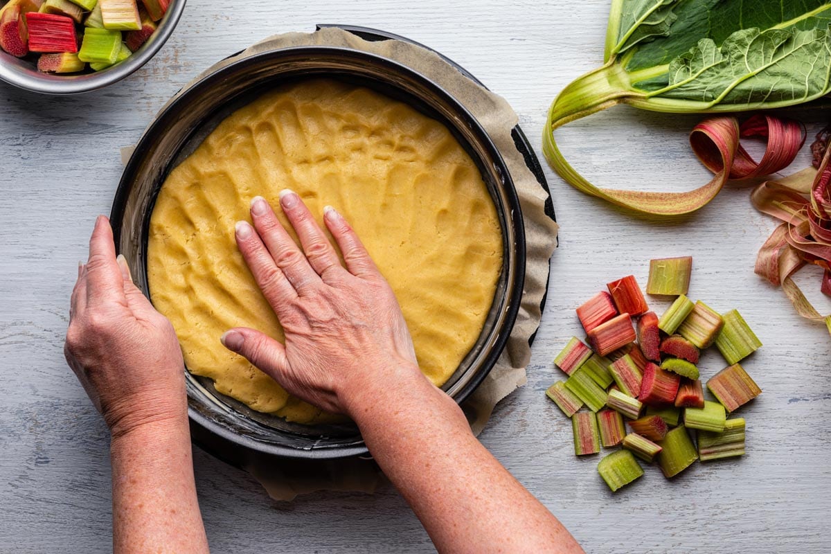 Two hands preparing a rhubarb dish in a round tin. 