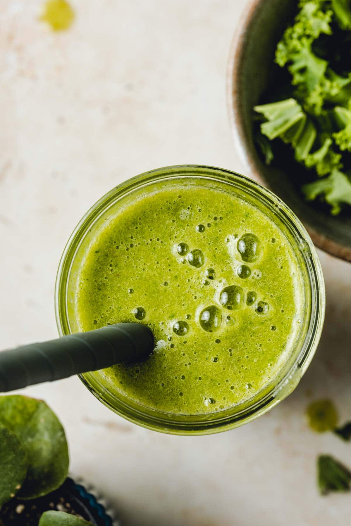 A close-up overhead image of green smoothie with a straw in the middle.