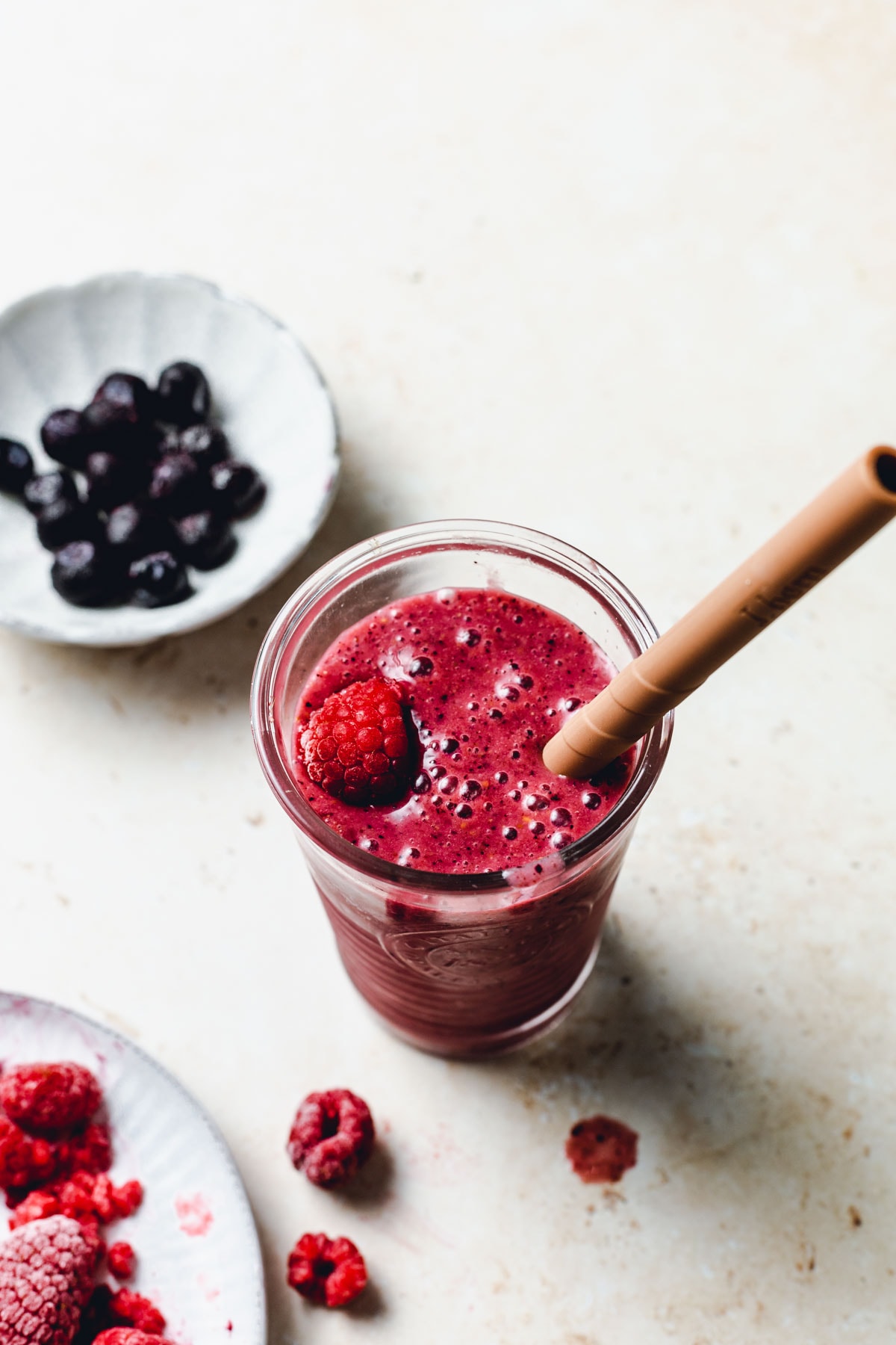 A side view of a deep red berry smoothie with blueberries and raspberries scattered around it.