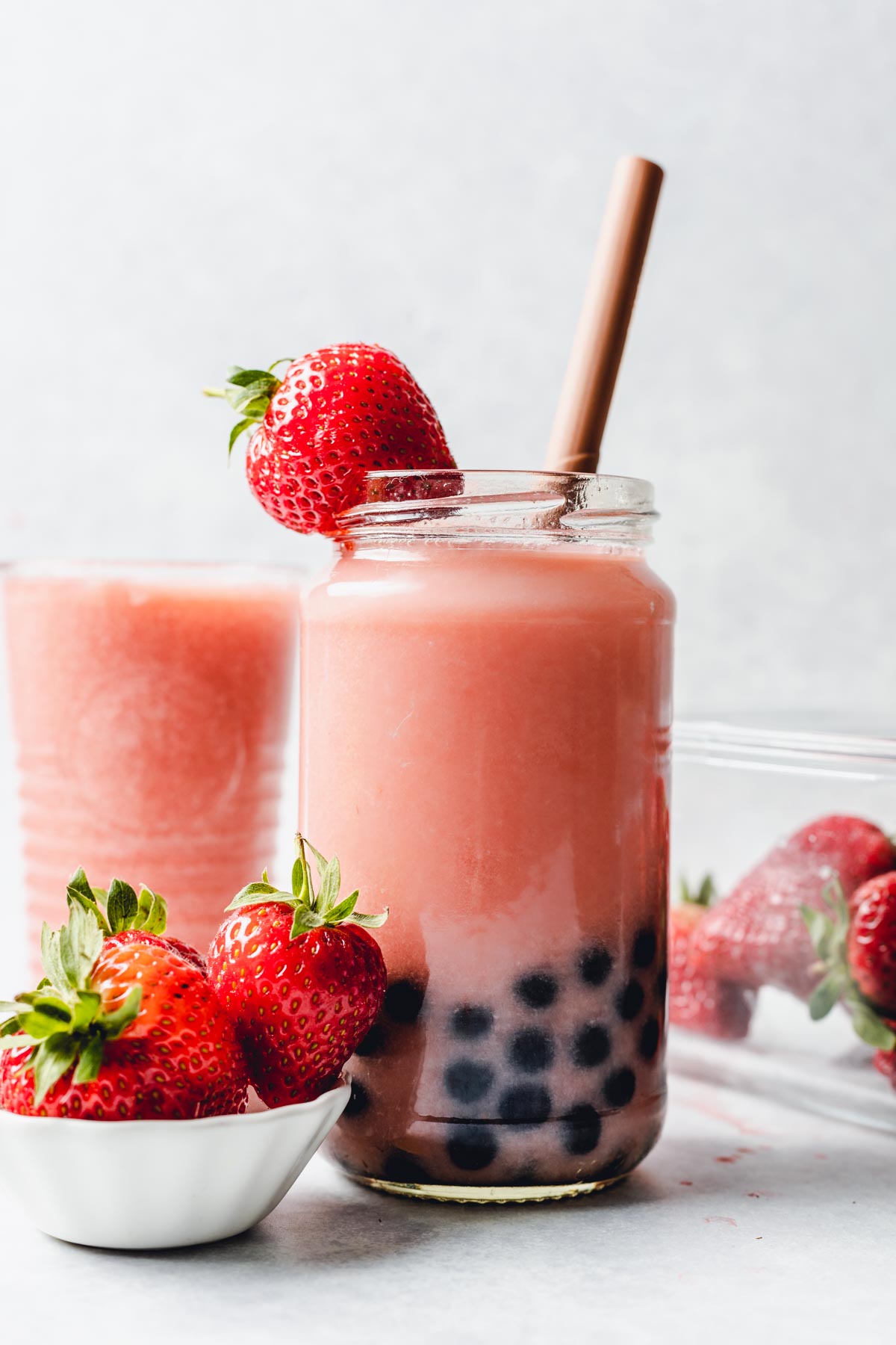 A glass filled with a pink drink with boba pearls at the bottom and strawberries around it.