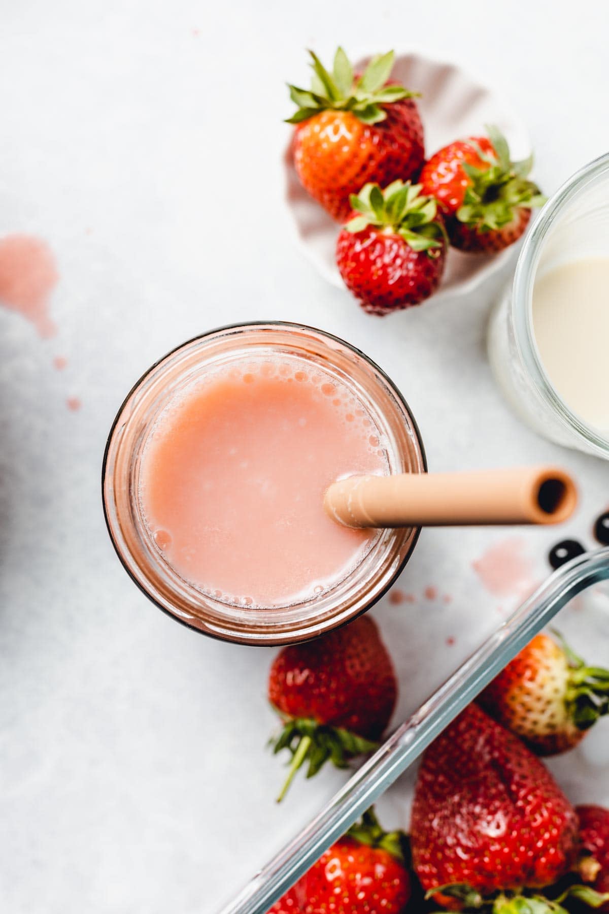 An overhead view of a glass of strawberry milk tea placed next to strawberries.