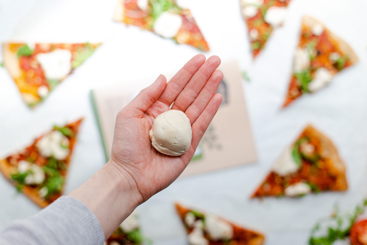 A hand holding out a ball of homemade vegan mozzarella style cheese.