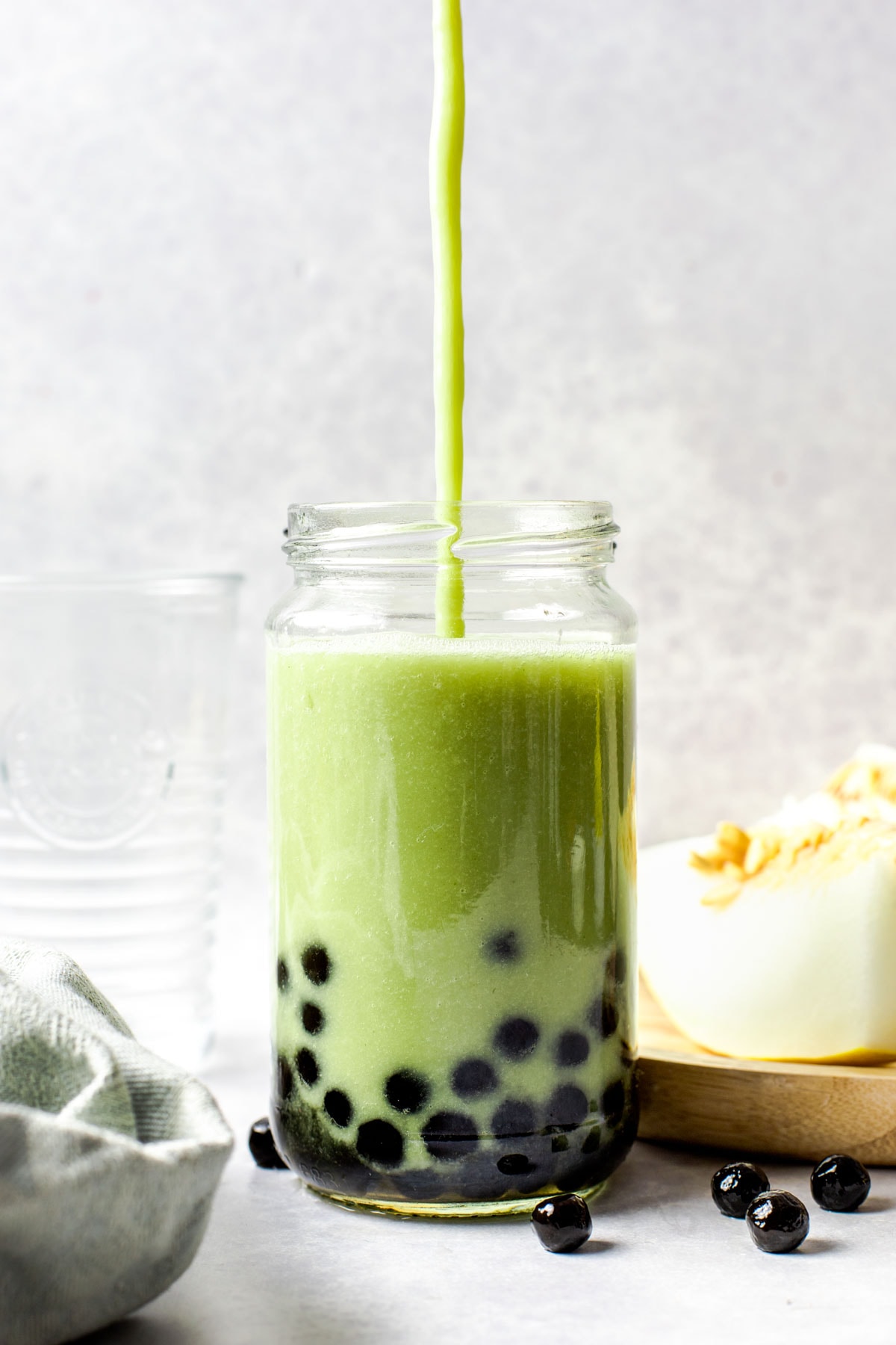 A green drink being poured into a tall glass containing black tapioca pearls.