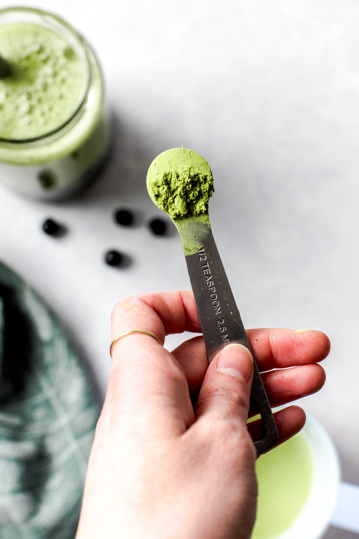 A hand holding a measuring spoon filled with matcha powder.