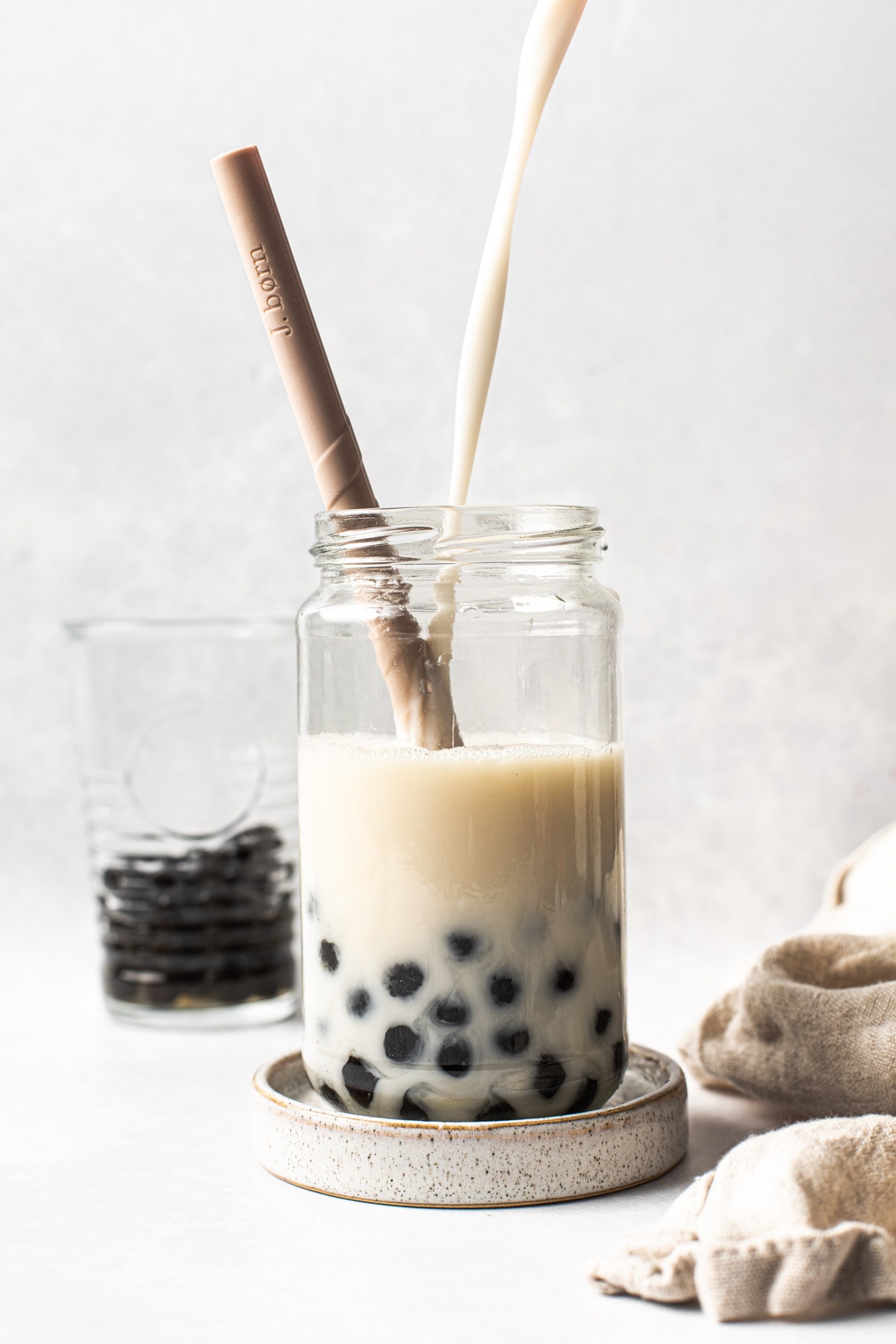 A side view of milk being poured into a glass containing black tapioca pearls.