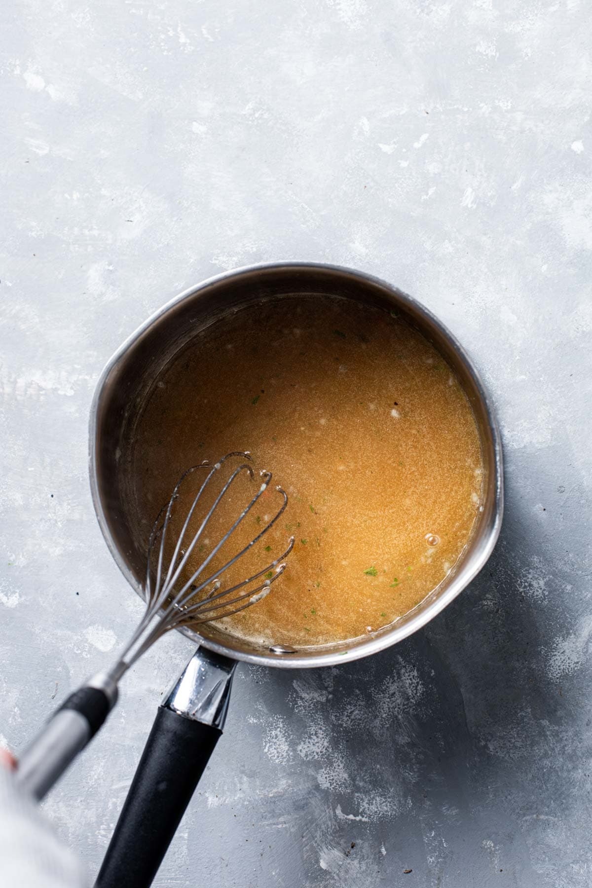 A saucepan containing keto gravy with a whisk inserted in the middle.