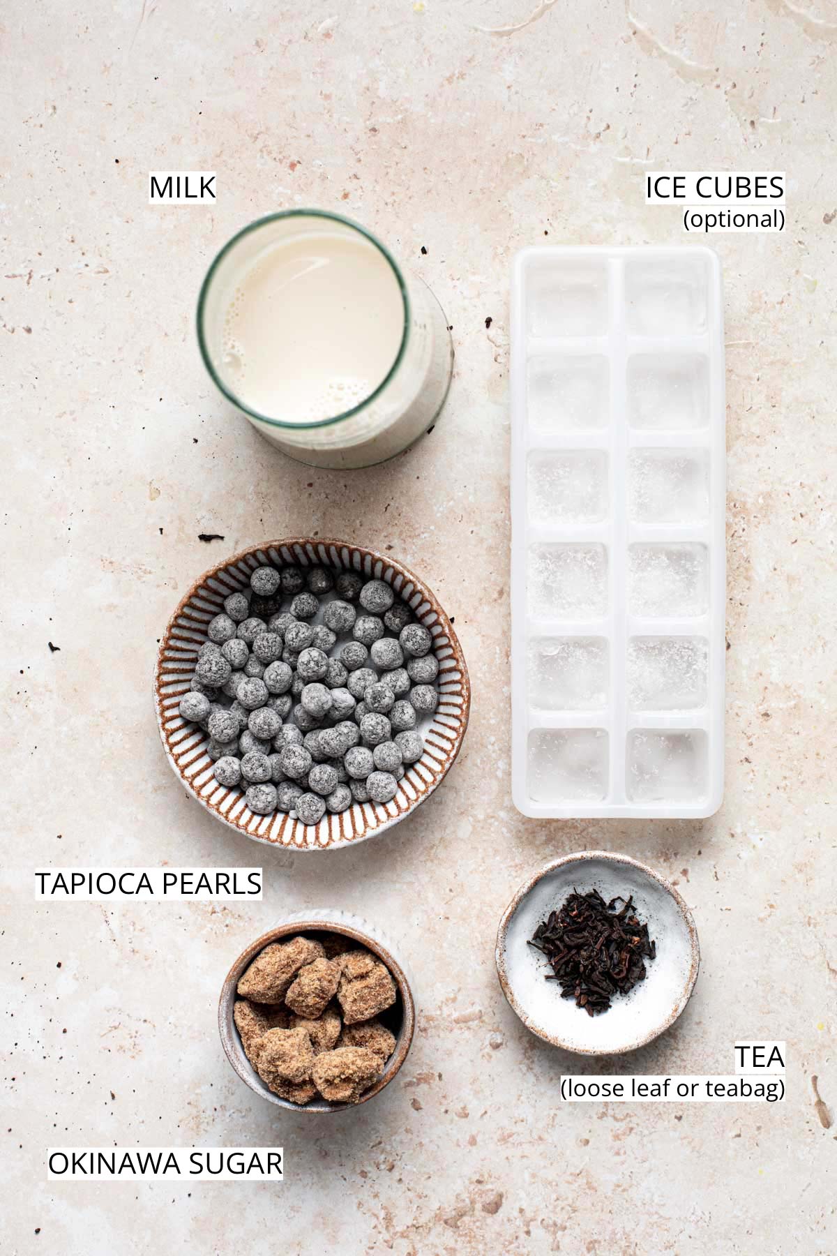 Milk, sugar, tea, ice cubes and tapioca pearls laid out on a flat surface.