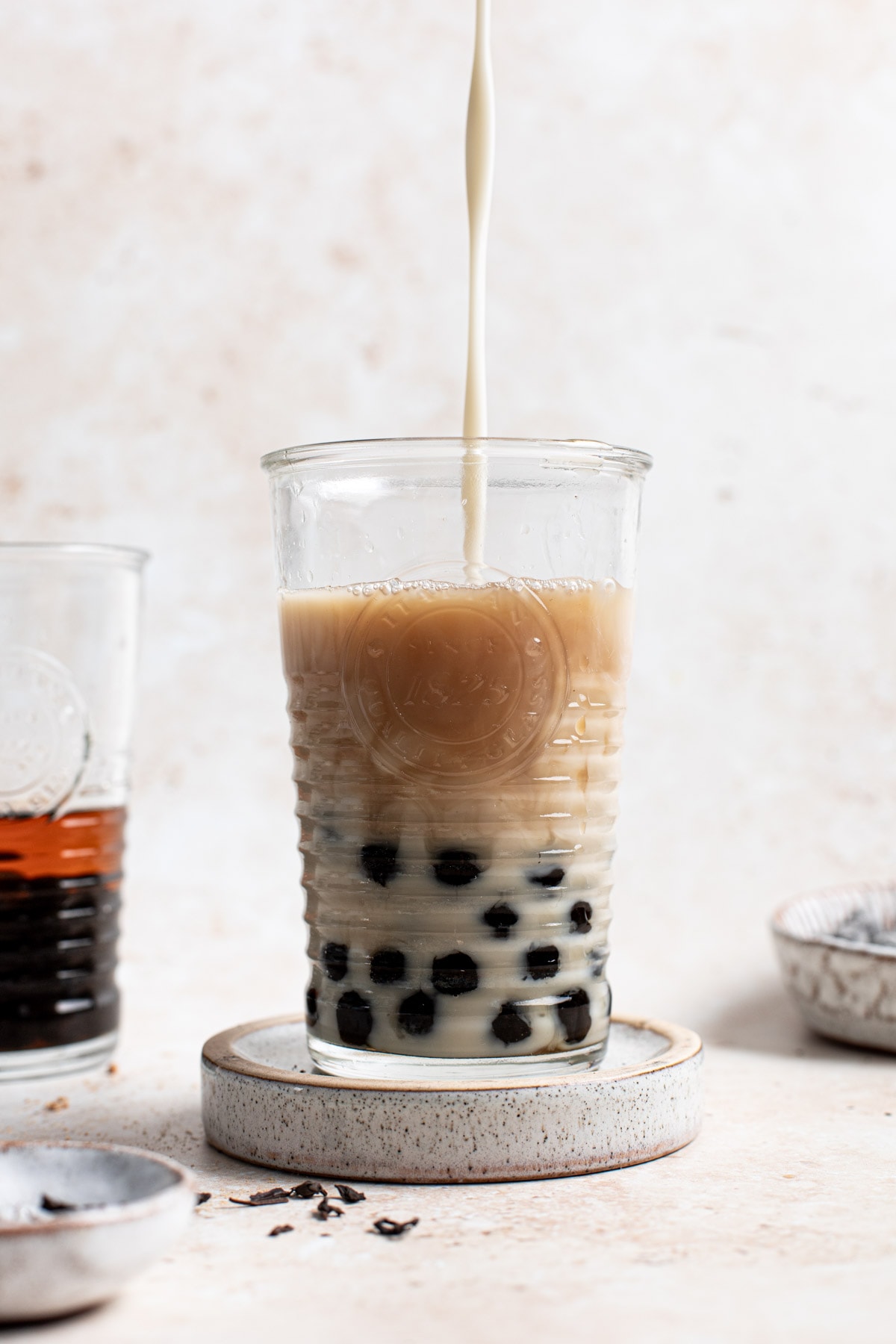 Milk being poured into a ribbed glass filled with boba pearls & tea.