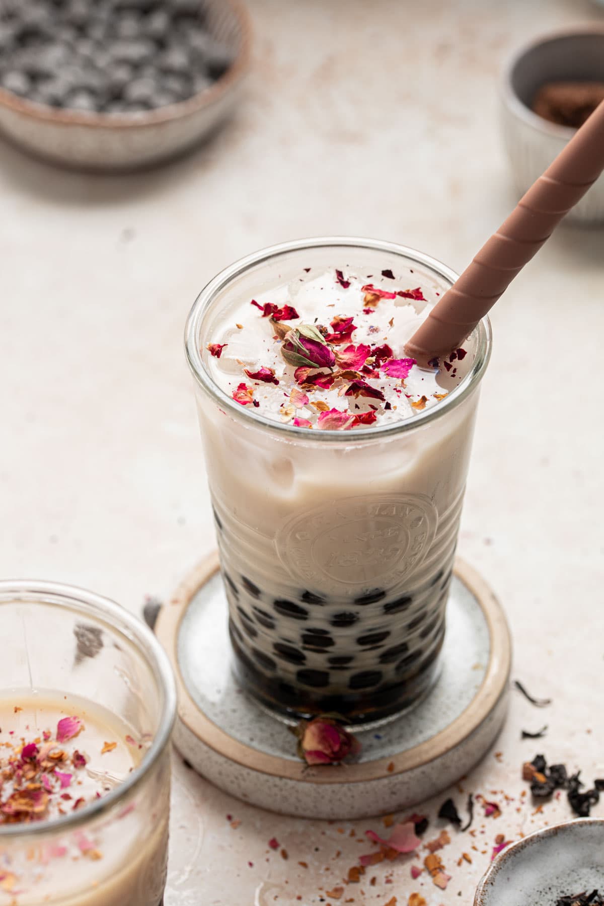 A glass filled with bubble tea and rose petals sprinkled on top.