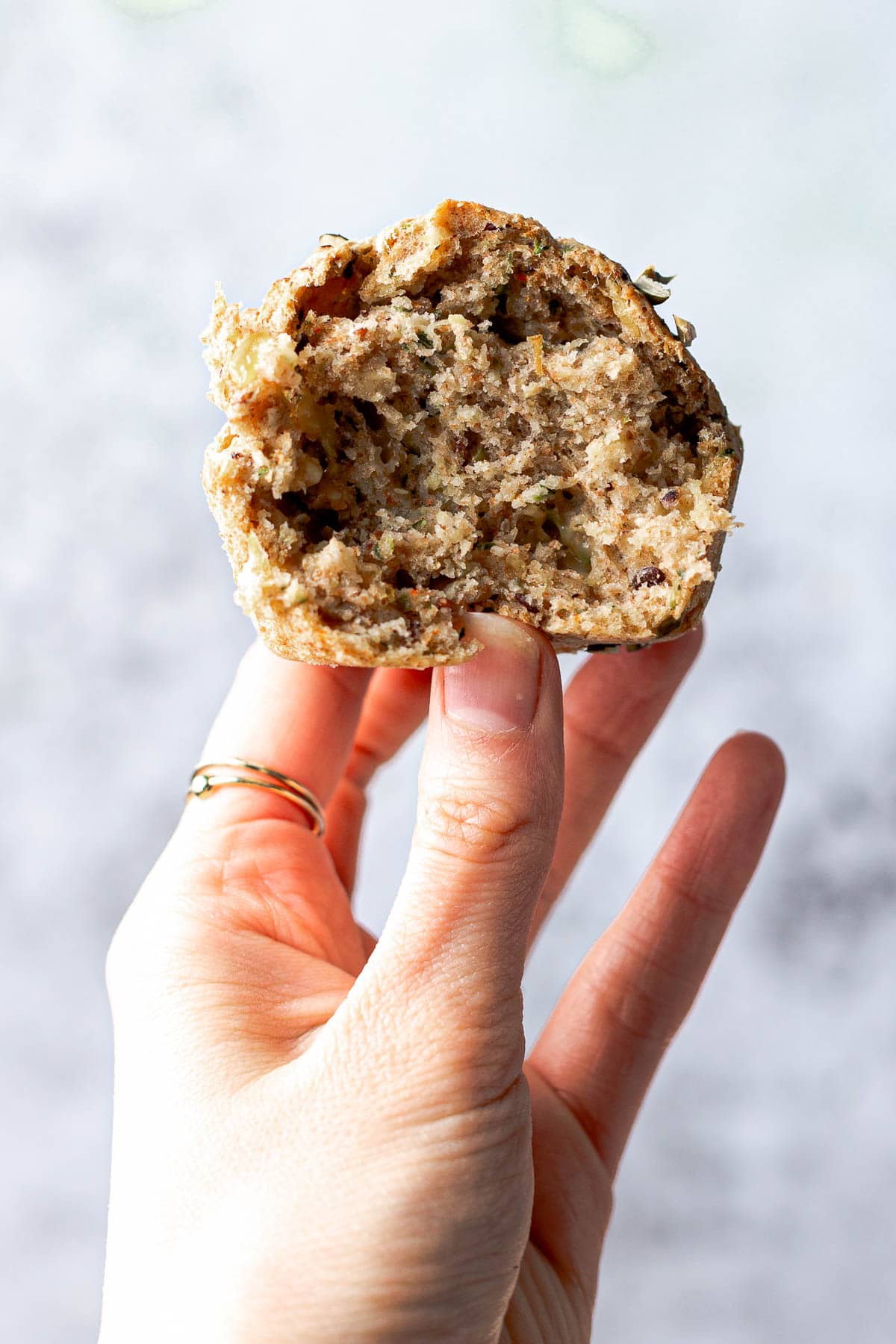 A hand holding a savoury vegan muffin with a bite taken out. 