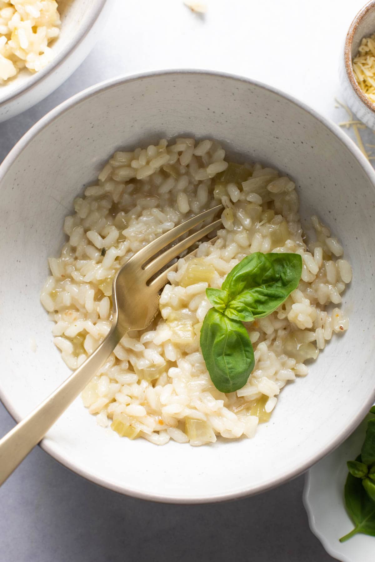 A bowl of risotto with a fork inserted in the middle and a few leaves of fresh basil on top.