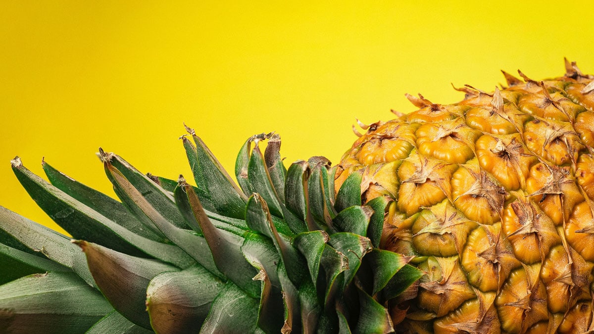 A whole pineapple lying on its side in front of a yellow background.