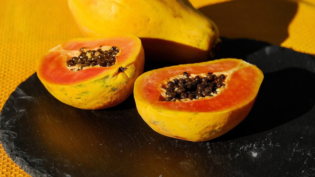 A papaya fruit cut in half and placed on a black surface.