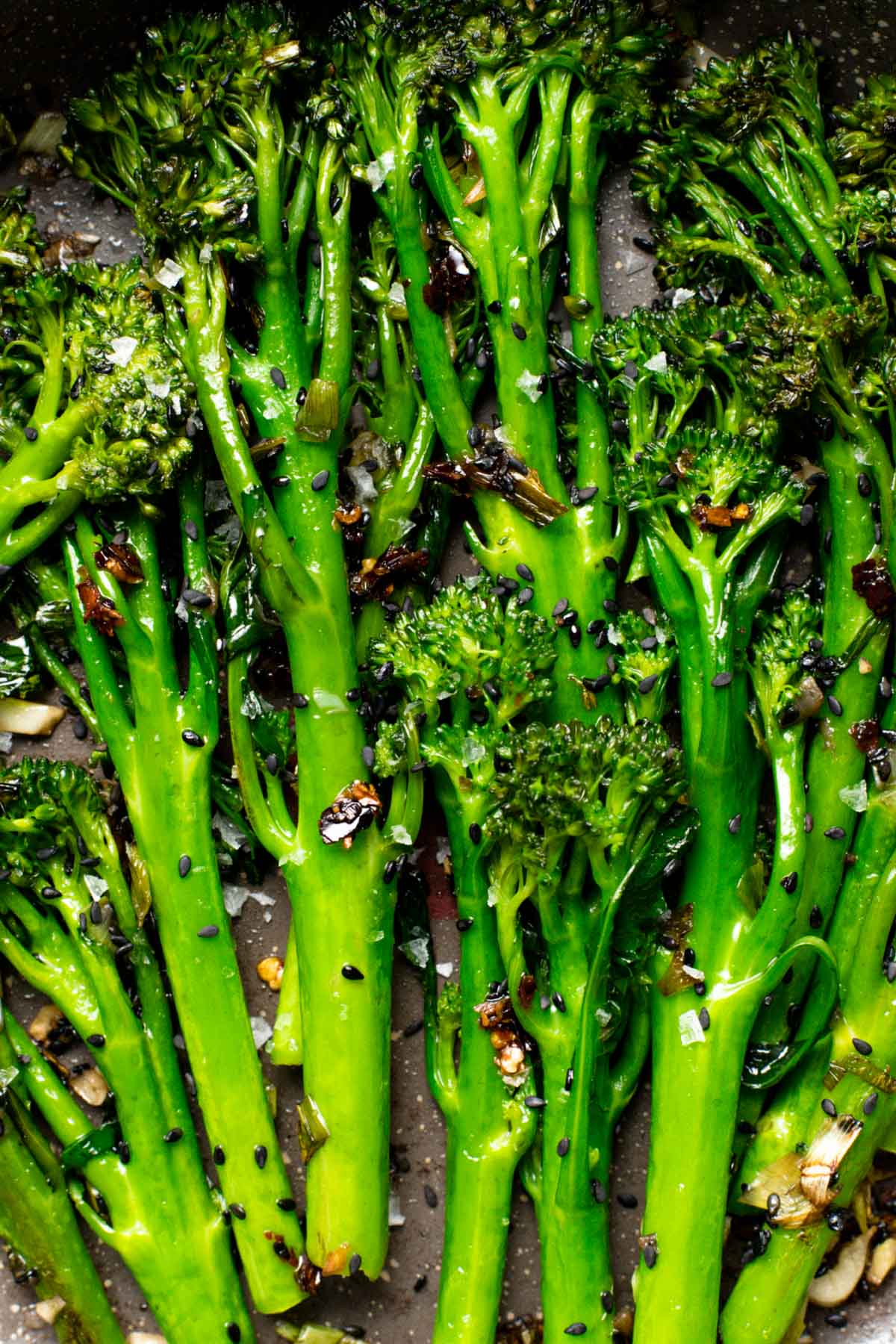 A very close-up, overhead image showing cooked broccolini with black sesame seeds. 