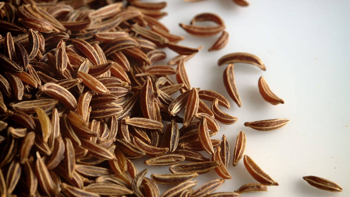 A close-up image of caraway seeds on a white background.